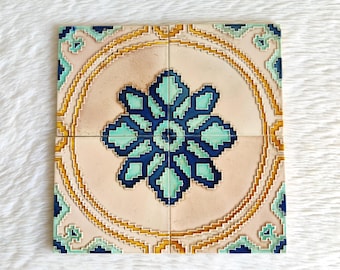 May include: Four square ceramic tiles with a floral design. The tiles are cream coloured with a blue and green floral pattern in the centre. The tiles are surrounded by a gold border.