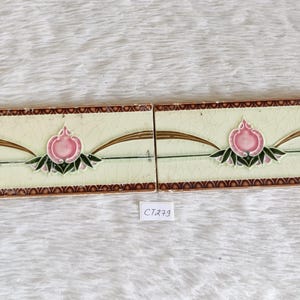 May include: Two vintage ceramic tiles with a brown border and a white background. Each tile features a pink flower with green leaves and a gold design.