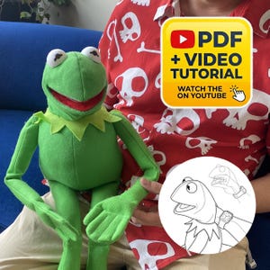 May include: A green plush frog puppet with a red mouth and a pointed collar. A yellow square graphic displays the text PDF + VIDEO TUTORIAL WATCH THE ON YOUTUBE with a YouTube icon. A circular line drawing shows a hand operating the frog puppet.