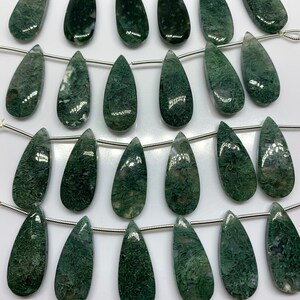 May include: A strand of 20 green moss agate teardrop beads, each with a unique pattern of green and white. The beads are strung on a silver chain with silver clasps.