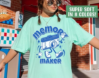 May include: A light blue t-shirt with a blue cartoon camera graphic and the text "Memory Maker". The text "Super Soft in 8 Colors!" is in a green box on the right side of the image.