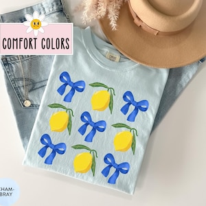 K&ouml;nnte beinhalten: Ein hellblaues T-Shirt mit einem Zitronen- und blauen Schleifenmuster. Das Shirt hat den Text "COMFORT COLORS" auf der Vorderseite.