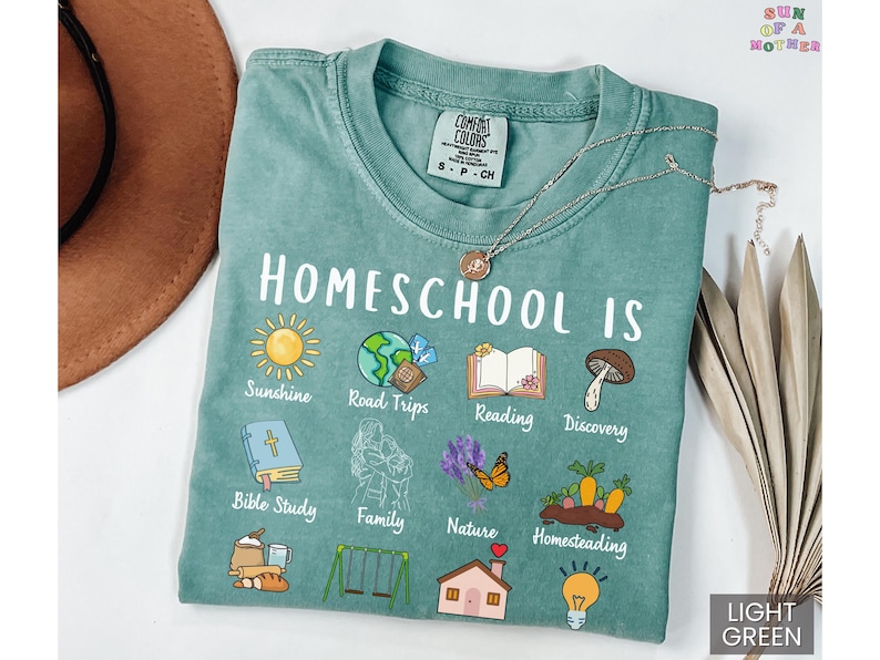 K&ouml;nnte beinhalten: Hellgr&uuml;nes T-Shirt mit der Aufschrift "Homeschool Is" und illustrierten Symbolen, die verschiedene Homeschooling-Themen darstellen. Das Shirt enth&auml;lt den Text "Sunshine, Road Trips, Reading, Discovery, Bible Study, Family, Nature, Homesteading."