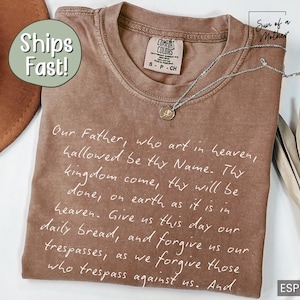 May include: A brown t-shirt with a white print of the Lord's Prayer. The shirt has a distressed look and is made of a soft, comfortable fabric.