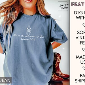 Puede incluir: Una camiseta azul vaquero con un gr&aacute;fico blanco de una persona con armadura y el texto "Put on the full armor of God Ephesians 6:10-18". La camiseta es suave y de estilo vintage.
