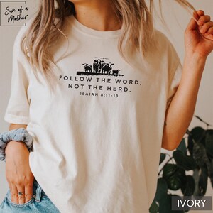 Peut inclure: Un t-shirt blanc avec un graphique noir d'un groupe de moutons et le texte "FOLLOW THE WORD, NOT THE HERD. ISAIAH 8:11-13".