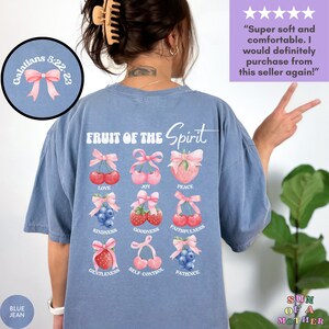 May include: A blue t-shirt with a white graphic of the "Fruit of the Spirit" with a pink bow on each fruit. The fruits are cherries, strawberries, and blueberries. The text "Galatians 5:22-23" is on the top left corner of the shirt.