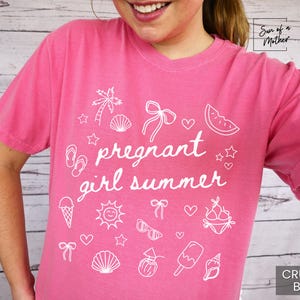 May include: A pink t-shirt with the text "pregnant girl summer" in white script, surrounded by white summer-themed illustrations. The shirt has short sleeves and a crew neck. The color is "Crunch-Berry".