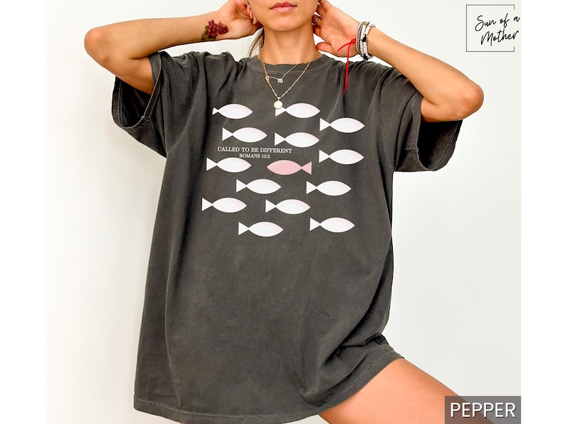 May include: A dark gray oversized t-shirt with a white graphic of fish. The text "Called to be Different" is printed on the shirt with the scripture reference "Romans 12:2".