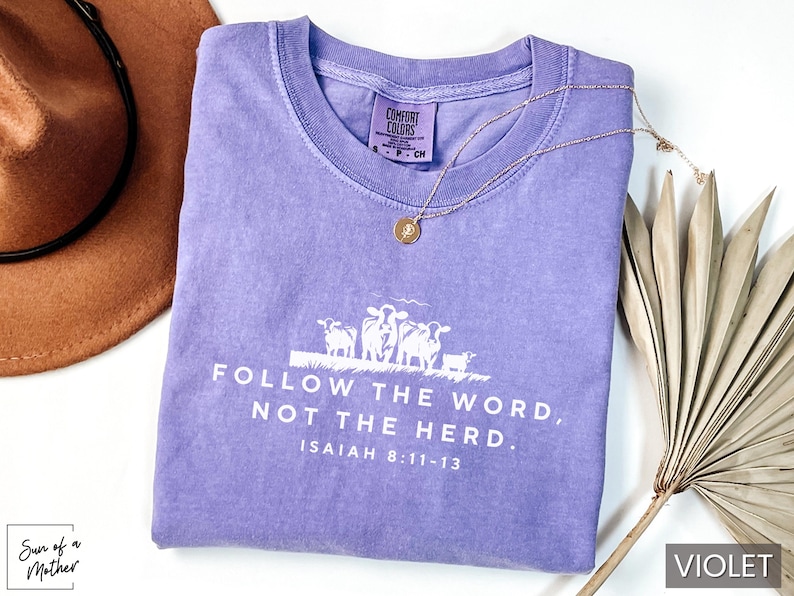 Peut inclure: T-shirt violet avec un graphique blanc de moutons et le texte "FOLLOW THE WORD, NOT THE HERD. ISAIAH 8:11-13".