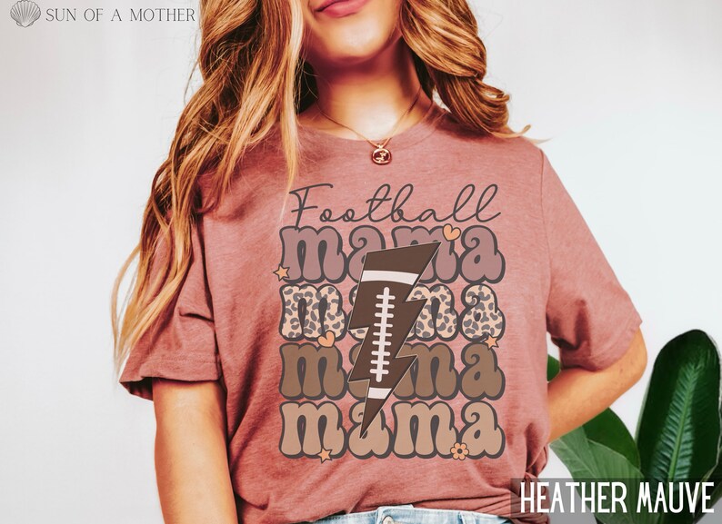 Puede incluir: Una camiseta de color malva brezo con el texto "Football Mama" en una fuente retro. El texto est&aacute; superpuesto con un estampado de leopardo marr&oacute;n y negro y un rayo marr&oacute;n con un bal&oacute;n de f&uacute;tbol en su interior.