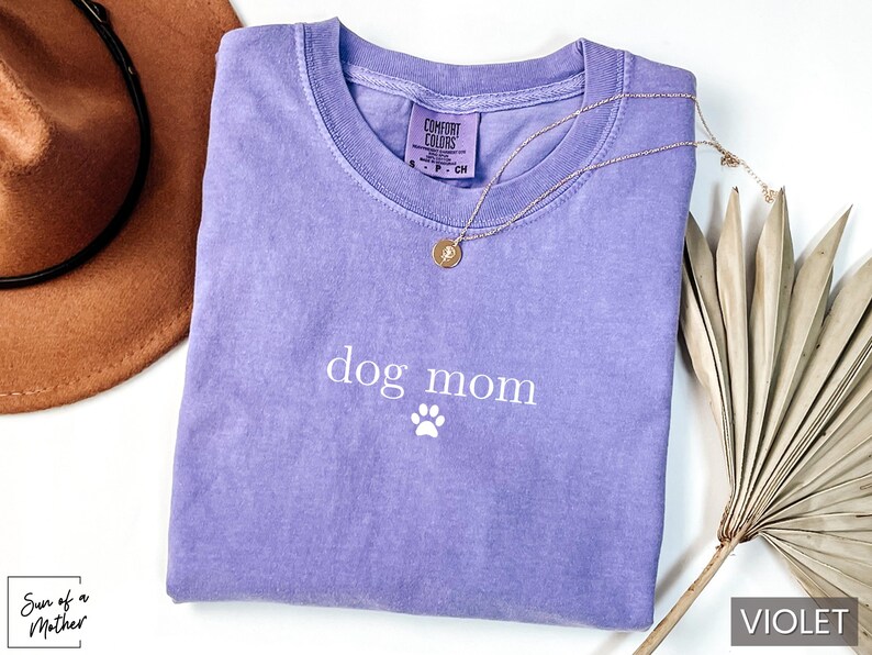 May include: A purple t-shirt with the text "dog mom" and a white paw print. The shirt is made of a soft, comfortable material.