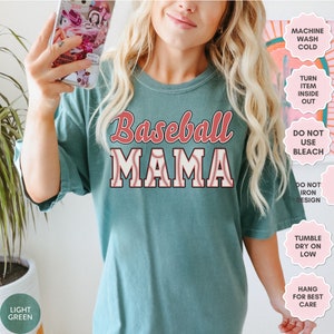 May include: A teal blue t-shirt with the text "Baseball Mama" in red and white. The text is surrounded by a baseball graphic. The shirt has care instructions printed on the right side of the image.