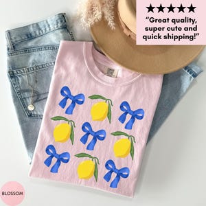 K&ouml;nnte beinhalten: Rosa T-Shirt mit einem Zitronen- und blauen Schleifenmuster. Das Shirt hat den Text "COMFORT COLORS" auf dem Etikett.