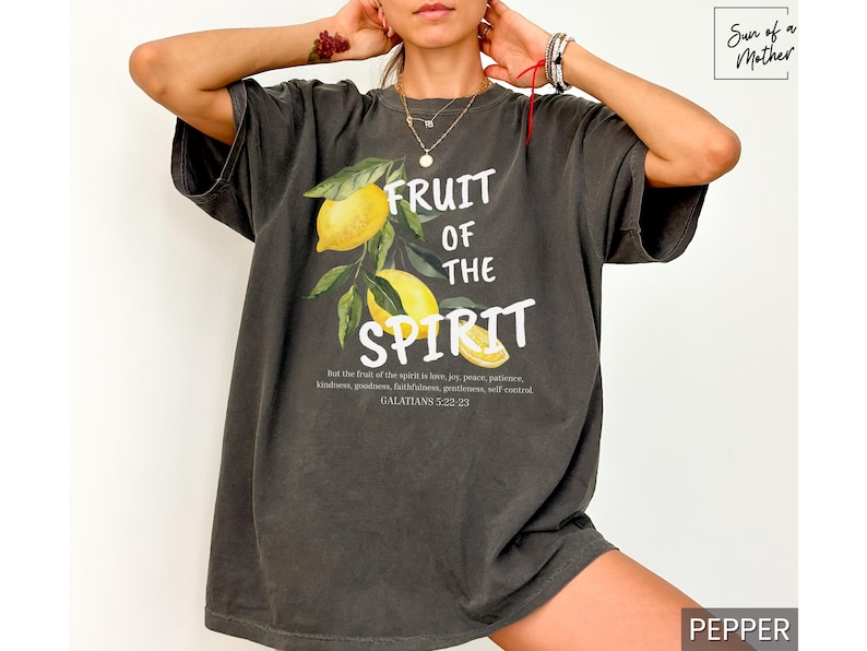 Op de afbeelding: Een donkergrijs T-shirt met een afbeelding van citroenen en de tekst "Fruit of the Spirit" en een bijbelvers uit Galaten 5:22-21.