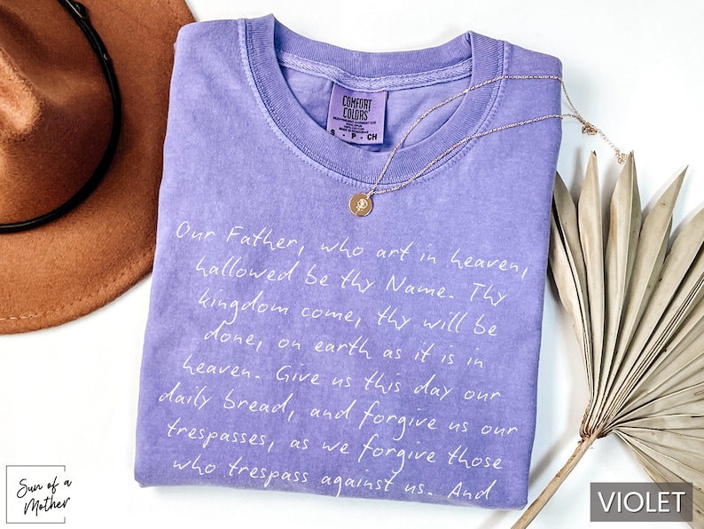 May include: A purple t-shirt with a white print of the Lord's Prayer. The shirt is made of a soft, comfortable fabric and has a relaxed fit.