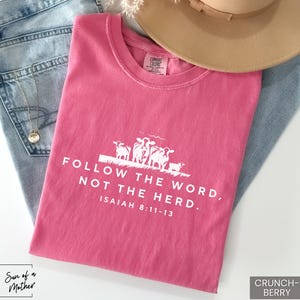 Peut inclure: T-shirt rose avec un texte blanc qui dit "Suivez la parole, pas le troupeau. Esa&iuml;e 8:11-13". Le t-shirt pr&eacute;sente un graphique de quatre moutons.
