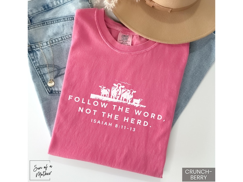 Peut inclure: T-shirt rose avec un texte blanc qui dit "Suivez la parole, pas le troupeau. Esa&iuml;e 8:11-13". Le t-shirt pr&eacute;sente un graphique de quatre moutons.