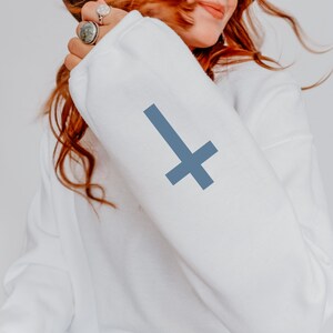 May include: White sweatshirt with a blue inverted cross on the sleeve.