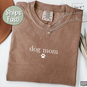 May include: A brown t-shirt with the text "dog mom" and a paw print in white. The shirt has a distressed look and is made of a soft, comfortable fabric.