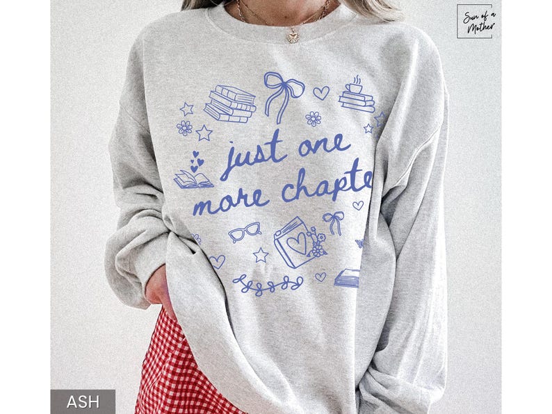 May include: Light gray sweatshirt with blue illustrations of books, hearts, and bows. The text "just one more chapter" is written in blue script. The sweatshirt is a casual style, perfect for book lovers.