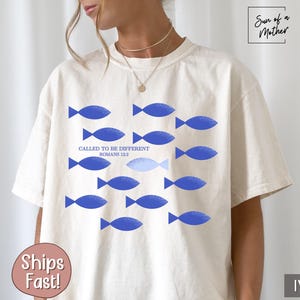 May include: A white t-shirt with a blue fish design and the text "Called to be different Romans 12:2".
