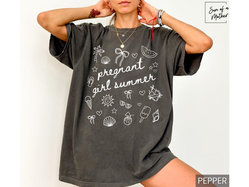 May include: Dark gray t-shirt with the phrase "pregnant girl summer" in white script, surrounded by summer-themed doodles. The shirt has a relaxed fit and short sleeves. The word "pepper" is in the bottom right corner.