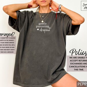 Puede incluir: Camiseta gris oscuro con la frase "gentle parenting dropout" en escritura blanca. La camiseta tiene un corte holgado y forma parte de una colecci&oacute;n de ropa. La imagen tambi&eacute;n incluye texto sobre la pol&iacute;tica de la tienda.