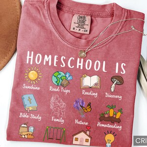 K&ouml;nnte beinhalten: Karmesinrotes T-Shirt mit der Aufschrift "Homeschool Is" und verschiedenen Illustrationen, darunter eine Sonne, ein Globus, ein Buch und ein Pilz. Das Shirt zeigt auch den Text "Sunshine, Road Trips, Reading, Discovery, Bible Study, Family, Nature, Homesteading."