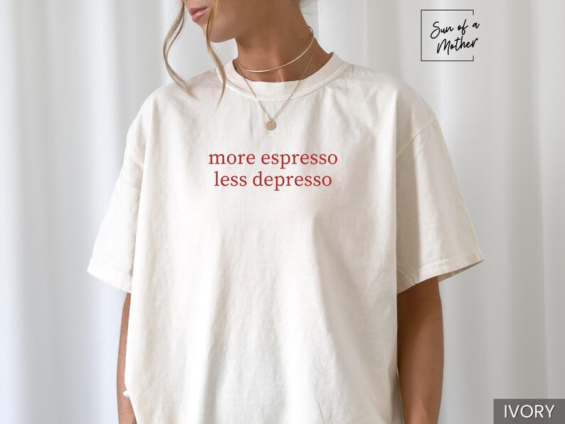 Op de afbeelding: Ivoor kleurig t-shirt met de rode tekst "more espresso less depresso". Het shirt heeft een relaxte pasvorm en korte mouwen. Het merklogo "Sun of a Mother" staat rechtsboven.
