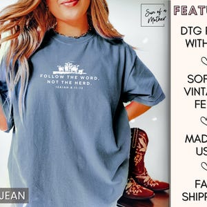Peut inclure: Un t-shirt bleu jean avec un texte blanc qui dit "Suivez la parole, pas le troupeau. Esa&iuml;e 8:11-13". Le t-shirt pr&eacute;sente un petit graphique de moutons. Le texte "Surf of a Mother" est visible dans le coin sup&eacute;rieur droit de l'image.