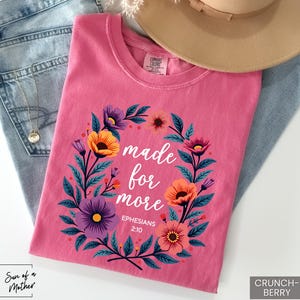 K&ouml;nnte beinhalten: Pinkes T-Shirt mit einem floralen Kranzdesign und dem Text "made for more Ephesians 2:10".