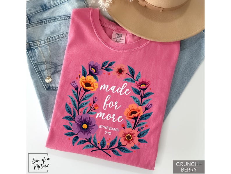 K&ouml;nnte beinhalten: Pinkes T-Shirt mit einem floralen Kranzdesign und dem Text "made for more Ephesians 2:10".
