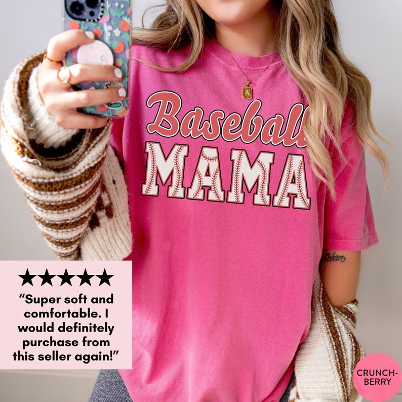 May include: Pink t-shirt with the text "Baseball Mama" in red and white lettering with a baseball stitch design. The text is in a vintage style font.