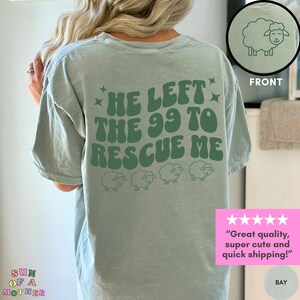 May include: A light green t-shirt with the text "He left the 99 to rescue me" in a retro font. There are five small sheep illustrations below the text. The shirt is displayed on a model.