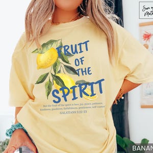 Op de afbeelding: Een geel T-shirt met een blauwe afbeelding waarop "Fruit of the Spirit" staat met citroenen en bladeren. De tekst onder de afbeelding luidt "But the fruit of the spirit is love, joy, peace, patience, kindness, goodness, faithfulness, gentleness, self control. Galatians 5:22-23".