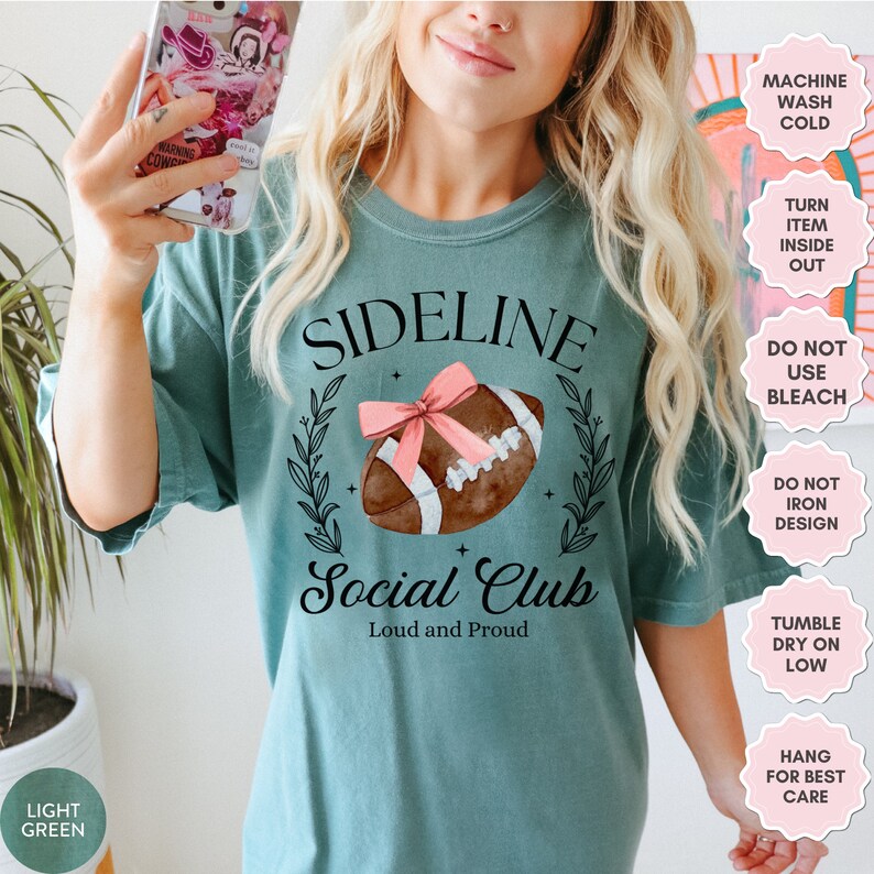 以下が含まれることがあります： ターコイズブルーのTシャツに、フットボールのグラフィックと「Sideline Social Club Loud and Proud」の文字がプリントされています。