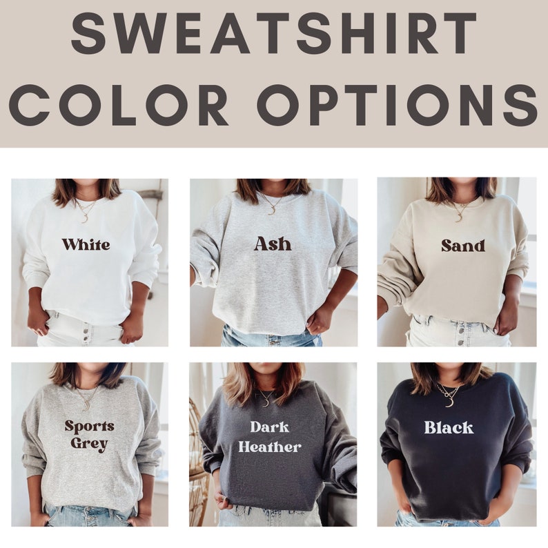 May include: Six different color options for a sweatshirt. The colors are white, ash, sand, sports grey, dark heather, and black. Each sweatshirt has the color name printed on the front.