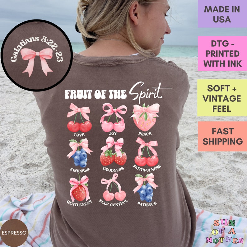 May include: A brown t-shirt with the text "Fruit of the Spirit" and a graphic of nine fruits with pink bows. The fruits are cherries, strawberries, and blueberries. The text "Galatians 5:22-23" is on a pink bow in the top left corner.