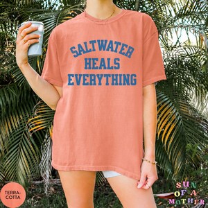 May include: A coral-colored t-shirt with the text "Saltwater Heals Everything" in blue.