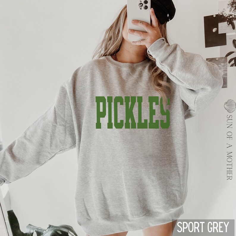 Op de afbeelding: Een grijs sweatshirt met het woord "PICKLES" in groene letters.