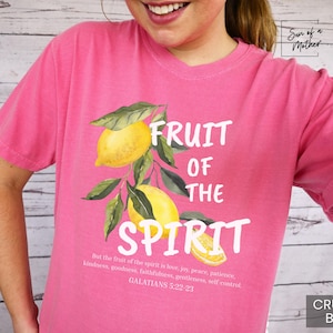 Op de afbeelding: Roze T-shirt met een witte afbeelding van citroenen en de tekst "Fruit of the Spirit" met een Bijbelvers uit Galaten 5:22-23.