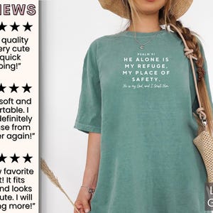 May include: Light green t-shirt with the text "PSALM 91 HE ALONE IS MY REFUGE, MY PLACE OF SAFETY. He is my God and I trust Him."  The shirt is being modeled by a person wearing a straw hat and a light brown bag.