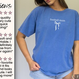 May include: A blue t-shirt with the text "football mom" and a bow graphic. The shirt is a solid color and appears to be made of a soft material. The shirt is a casual style.