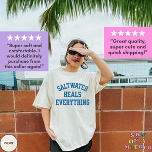 May include: A white t-shirt with the text "Saltwater Heals Everything" in blue lettering. The shirt is being worn by a person with sunglasses and a palm tree in the background. The text "IVORY" is visible in the lower left corner of the image.