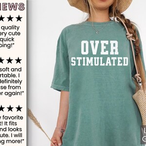 May include: A light green t-shirt with the text "OVER STIMULATED" in white. The shirt is made of a soft, comfortable material and is perfect for everyday wear.