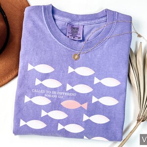 May include: A purple t-shirt with a white fish design and the text "Called to be different Romans 12:2".