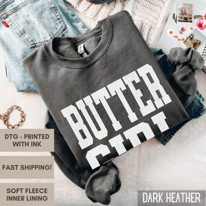 May include: Dark heather grey sweatshirt with the text "BUTTER CIN" printed in white.