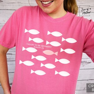 May include: Pink t-shirt with a white graphic of fish and the text "Called to be different Romans 12:2".
