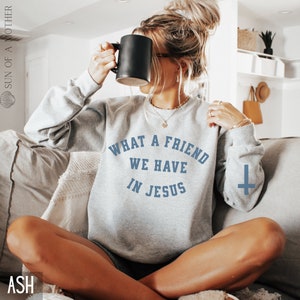 May include: A gray sweatshirt with the text "What a friend we have in Jesus" in blue lettering. A small cross is printed on the right sleeve.